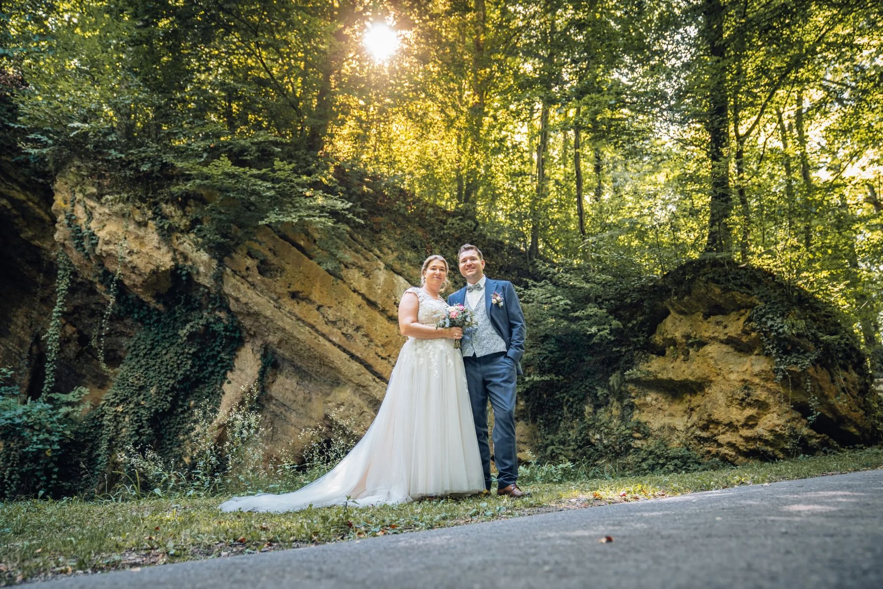 Brautpaar auf einem Waldweg vor einer Felswand im Abendlicht